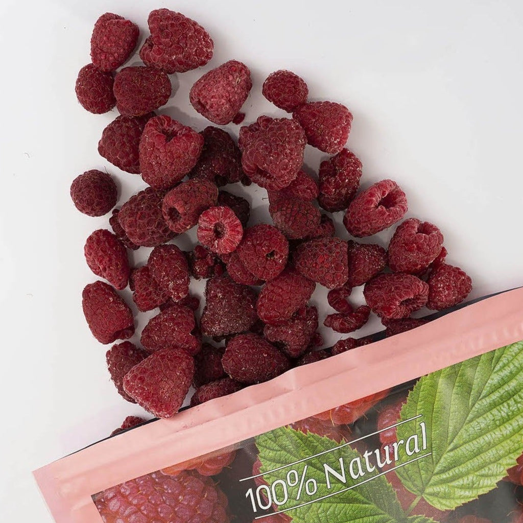 raspberries spilled from a pink bag labeled '100% Natural' and 'raspberries' on a white background.